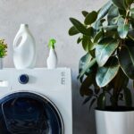 detergent and spray bottles on washing machine near plants in bathroom
