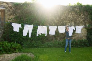 Woman standing on a lawn in a garden, hanging up laundry on washing line.